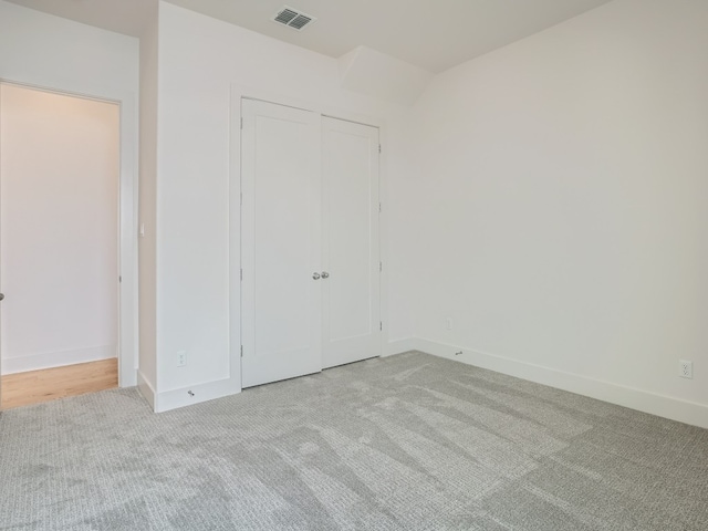 unfurnished bedroom featuring light colored carpet, a closet, visible vents, and baseboards