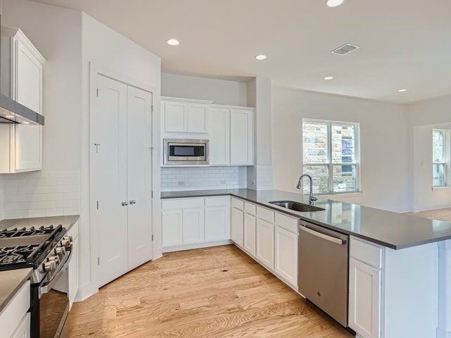 kitchen with light wood finished floors, visible vents, appliances with stainless steel finishes, a peninsula, and a sink