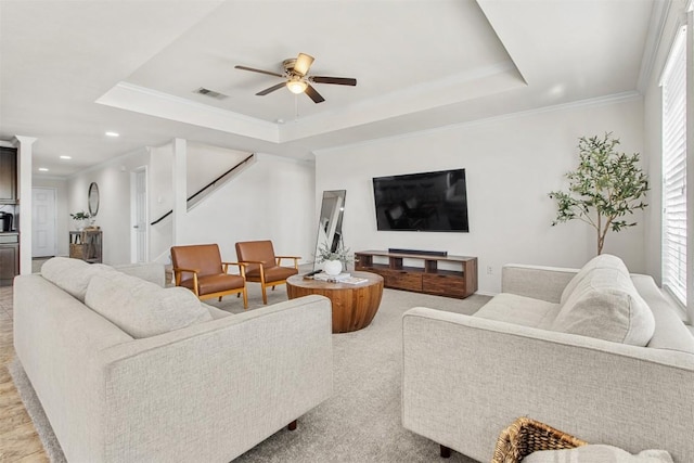 living room with ornamental molding, a tray ceiling, visible vents, and stairs