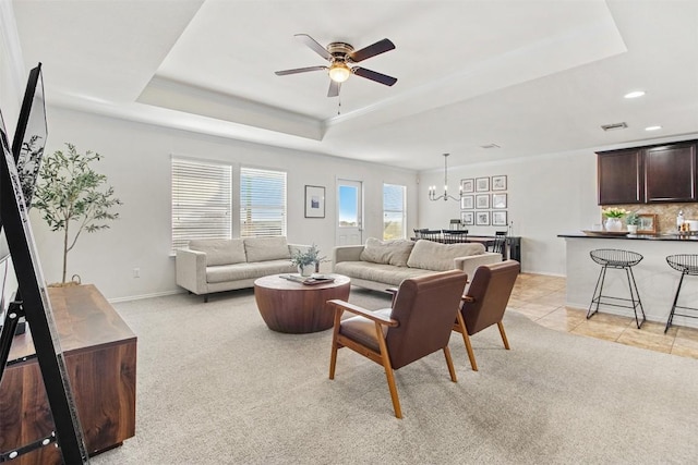 living area featuring ceiling fan with notable chandelier, a tray ceiling, light carpet, and light tile patterned flooring