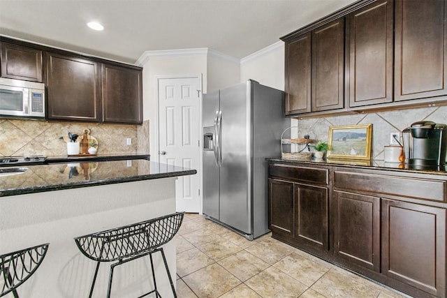 kitchen featuring stainless steel appliances, ornamental molding, dark stone countertops, and dark brown cabinetry