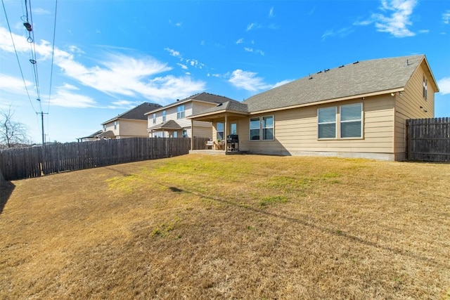 back of house featuring a patio area, a fenced backyard, a shingled roof, and a yard