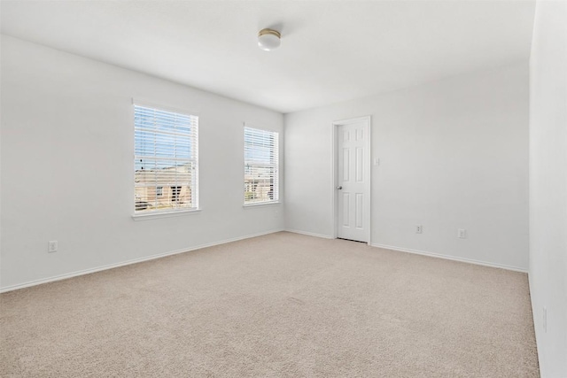 spare room featuring light carpet and baseboards