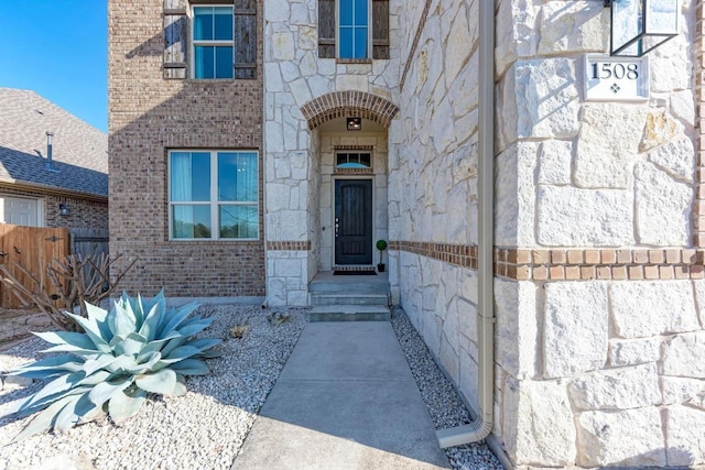 doorway to property with fence, brick siding, and stone siding