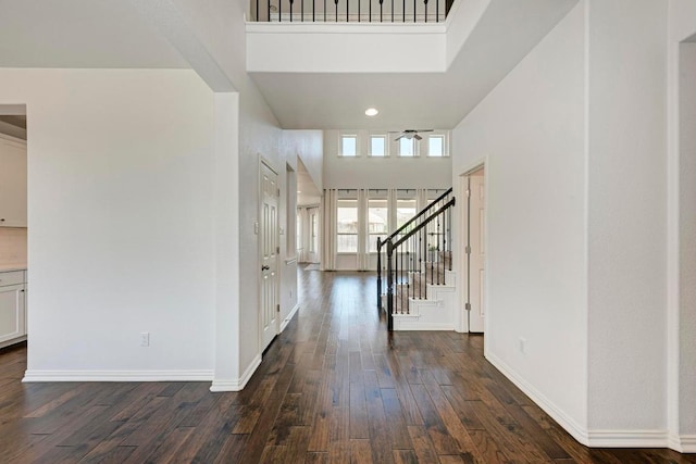 entryway featuring dark wood finished floors, stairs, baseboards, a ceiling fan, and a high ceiling