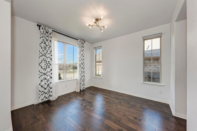 empty room with a notable chandelier, dark wood finished floors, and baseboards