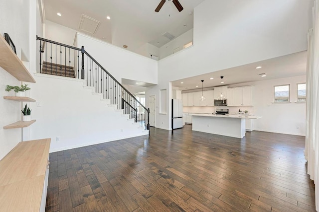 unfurnished living room with a high ceiling, a ceiling fan, stairway, and dark wood finished floors