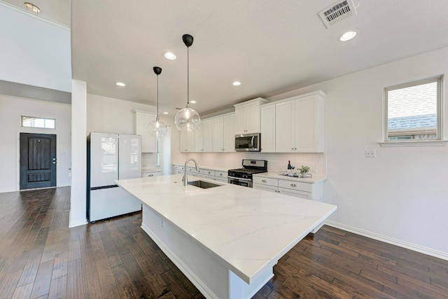 kitchen with a kitchen island with sink, a sink, stainless steel appliances, white cabinets, and dark wood finished floors