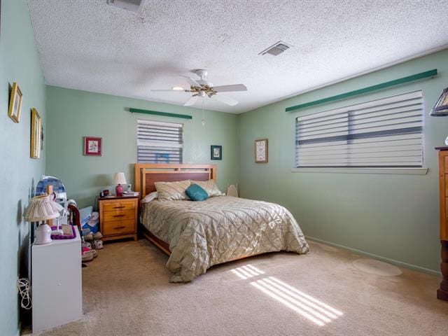 carpeted bedroom featuring visible vents, ceiling fan, a textured ceiling, and baseboards