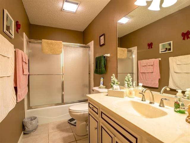 full bath with a textured ceiling, enclosed tub / shower combo, toilet, vanity, and tile patterned floors