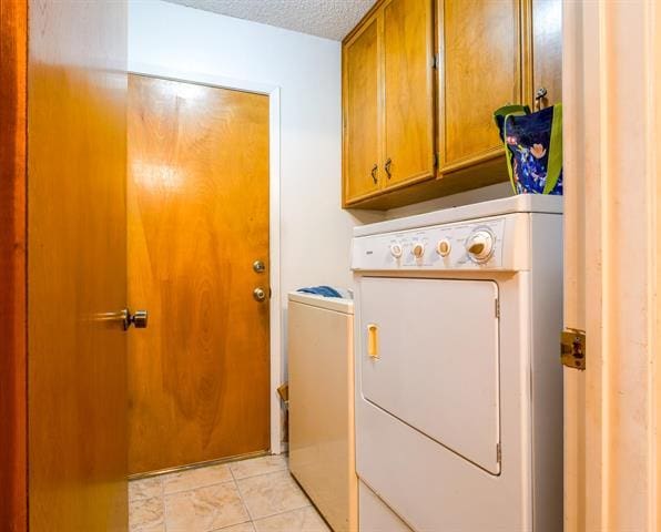 clothes washing area featuring light tile patterned floors, washer and clothes dryer, a textured ceiling, and cabinet space