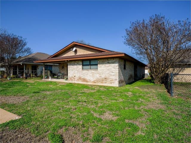 rear view of house featuring a patio, brick siding, a lawn, and fence