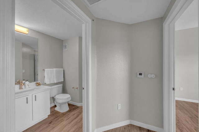 bathroom featuring baseboards, visible vents, toilet, wood finished floors, and vanity