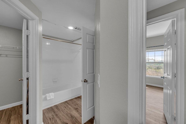 bathroom with a textured wall, shower / tub combination, baseboards, and wood finished floors