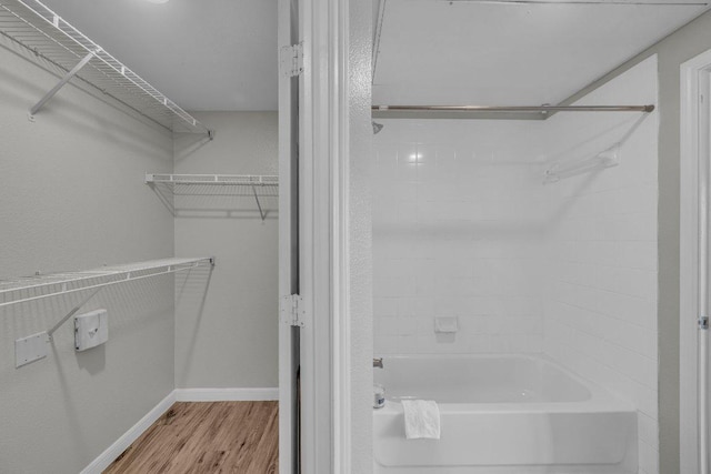 bathroom featuring a walk in closet, tub / shower combination, baseboards, and wood finished floors