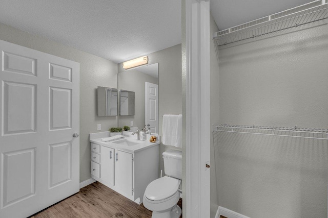 bathroom featuring toilet, a textured ceiling, vanity, wood finished floors, and baseboards