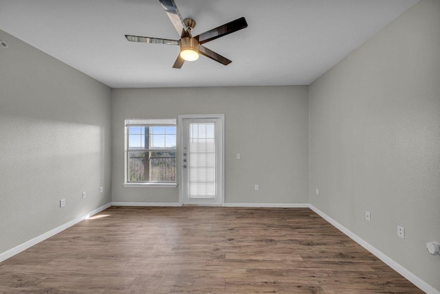 spare room with wood finished floors, a ceiling fan, and baseboards