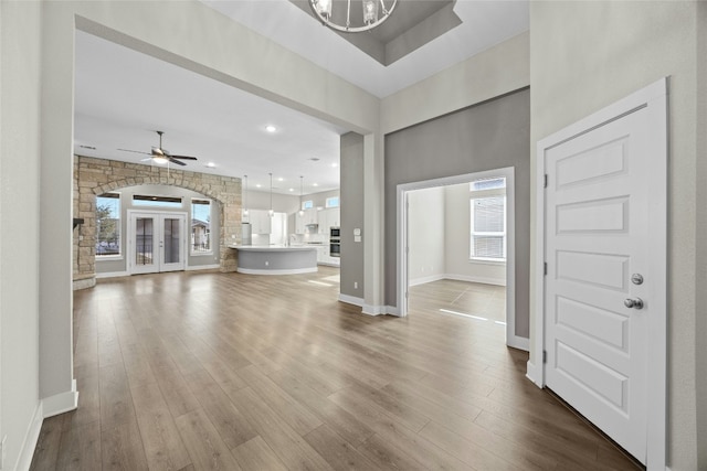 unfurnished living room with arched walkways, recessed lighting, ceiling fan with notable chandelier, baseboards, and dark wood finished floors