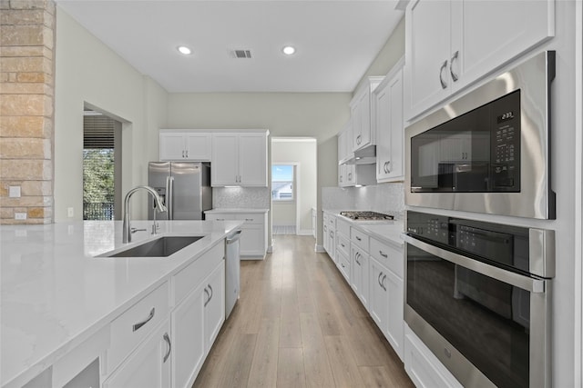 kitchen with stainless steel appliances, visible vents, decorative backsplash, a sink, and light wood-type flooring