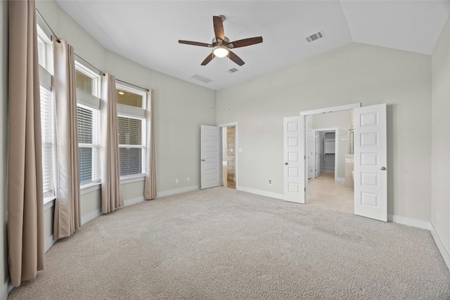 unfurnished bedroom featuring light carpet, baseboards, visible vents, vaulted ceiling, and a walk in closet