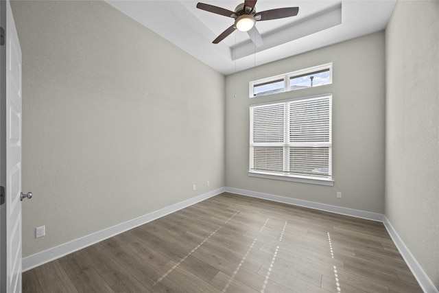 empty room featuring a ceiling fan, a tray ceiling, dark wood-style flooring, and baseboards