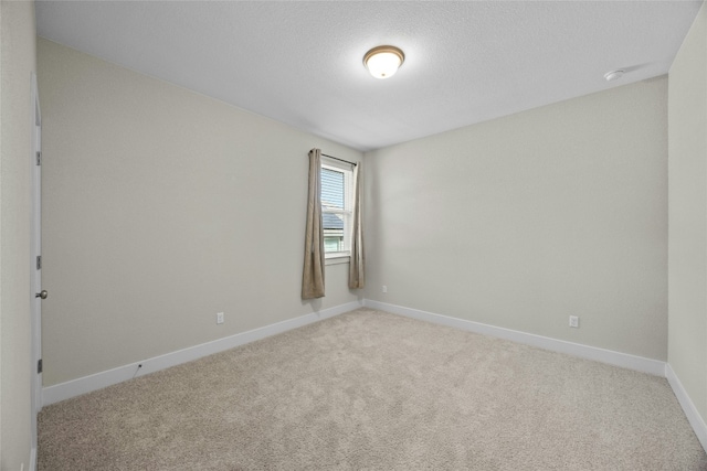 spare room with baseboards, a textured ceiling, and light colored carpet