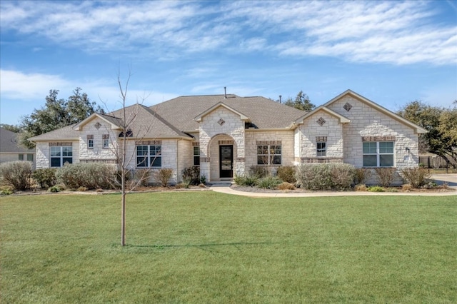 french country home featuring stone siding, a shingled roof, and a front yard