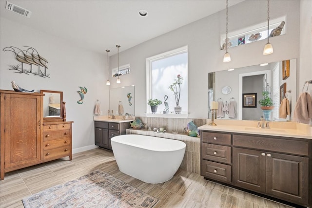 bathroom featuring a freestanding tub, two vanities, a sink, and visible vents