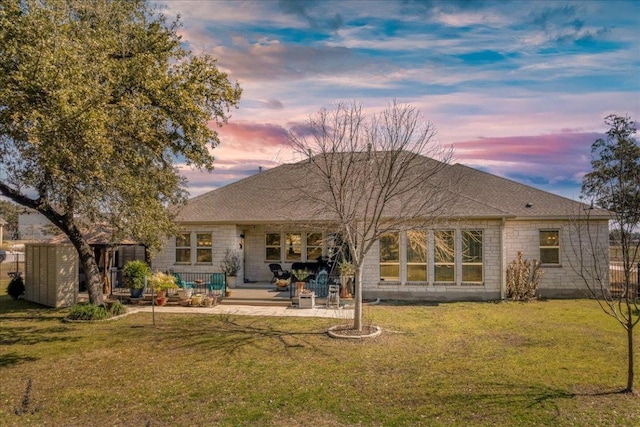 back of house with a yard, a shingled roof, a patio area, and stone siding