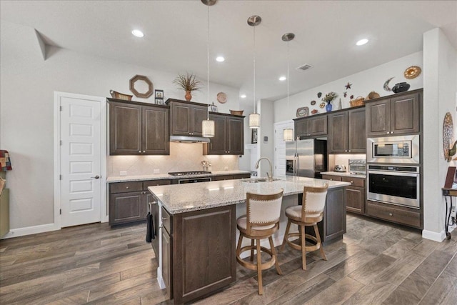 kitchen with a center island with sink, dark wood-style floors, appliances with stainless steel finishes, dark brown cabinets, and a sink