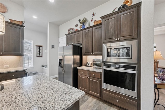 kitchen with dark brown cabinetry, light wood finished floors, decorative backsplash, light stone countertops, and stainless steel appliances