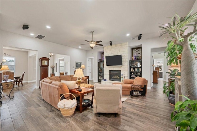 living area with recessed lighting, visible vents, ceiling fan, a stone fireplace, and wood finished floors