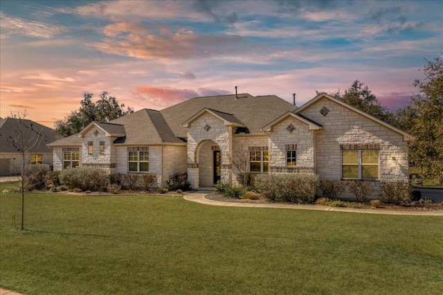 french country style house with a shingled roof, a front yard, and stone siding