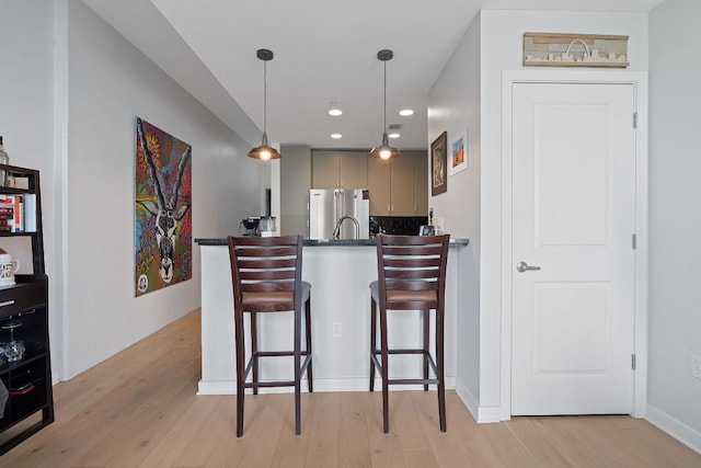 kitchen featuring a kitchen bar, stainless steel fridge, dark countertops, and light wood-style flooring