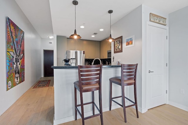 kitchen featuring dark countertops, freestanding refrigerator, a peninsula, and light wood-style flooring