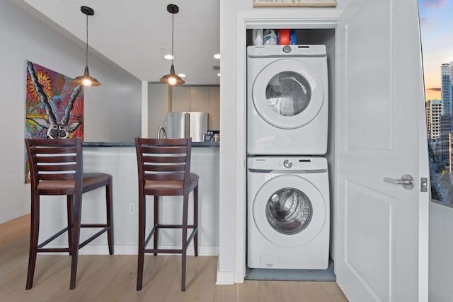 clothes washing area with light wood-style floors, laundry area, and stacked washer / dryer