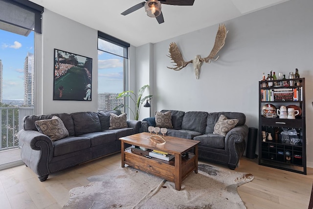 living area with a wall of windows, light wood-style floors, and ceiling fan