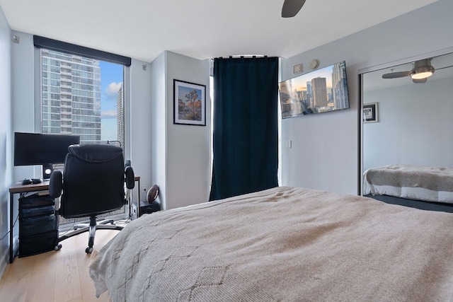 bedroom with a city view, ceiling fan, and wood finished floors