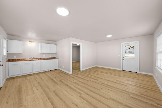 kitchen with light wood-type flooring, baseboards, white cabinetry, and a sink