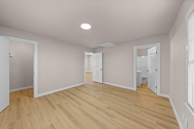 unfurnished bedroom featuring light wood finished floors, a spacious closet, baseboards, and connected bathroom