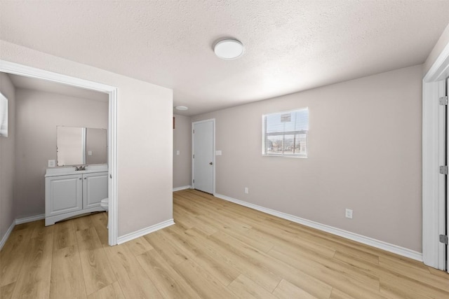 unfurnished room with a textured ceiling, light wood-type flooring, a sink, and baseboards