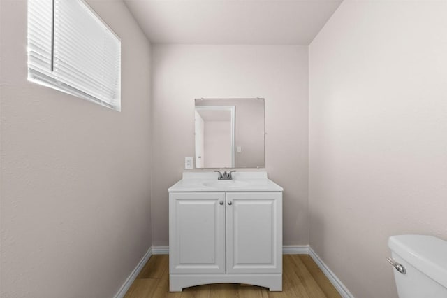 half bath with toilet, baseboards, wood finished floors, and vanity