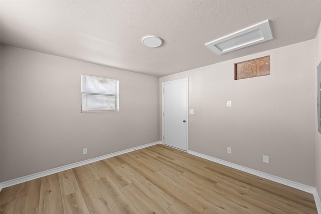 spare room with light wood-style flooring, a textured ceiling, attic access, and baseboards