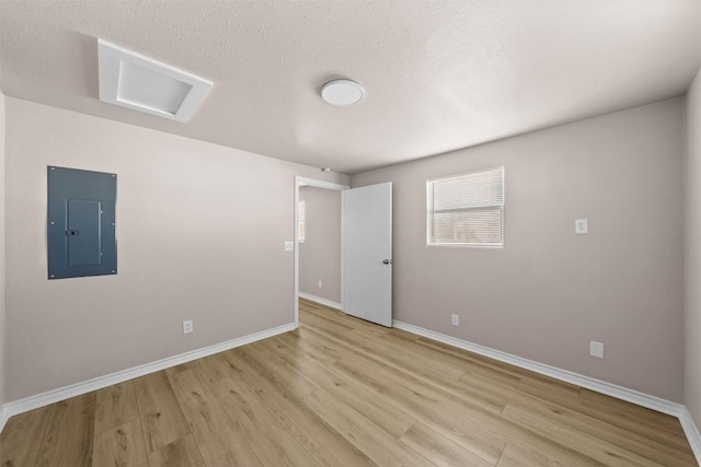 empty room featuring light wood finished floors, attic access, a textured ceiling, electric panel, and baseboards