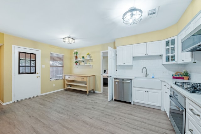 kitchen featuring stainless steel appliances, tasteful backsplash, light countertops, visible vents, and a sink