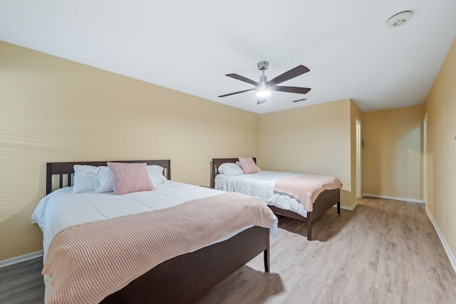 bedroom with light wood-style floors, ceiling fan, visible vents, and baseboards