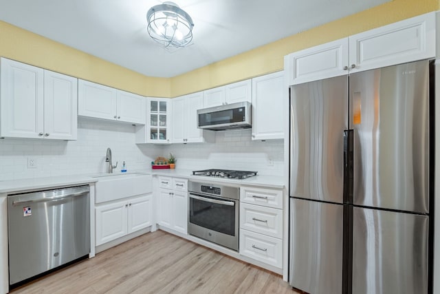 kitchen with stainless steel appliances, a sink, white cabinetry, light countertops, and light wood-type flooring