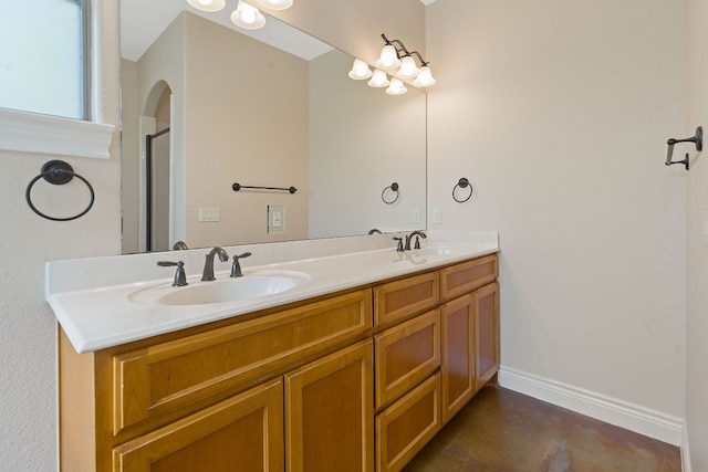 full bathroom with double vanity, a sink, a shower with shower door, and baseboards