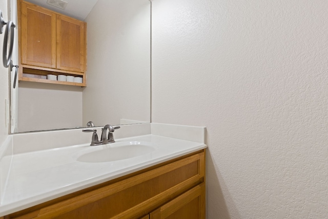 bathroom with visible vents, a textured wall, and vanity