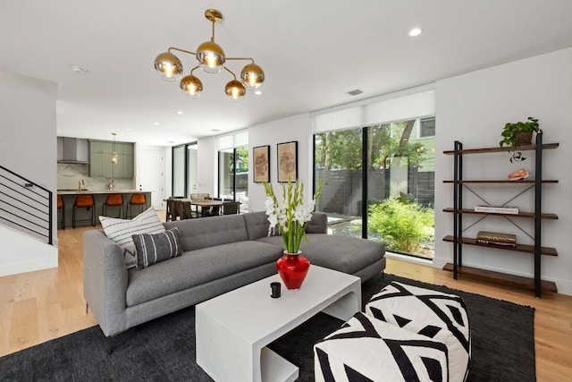 living area with visible vents, stairway, wood finished floors, a chandelier, and recessed lighting